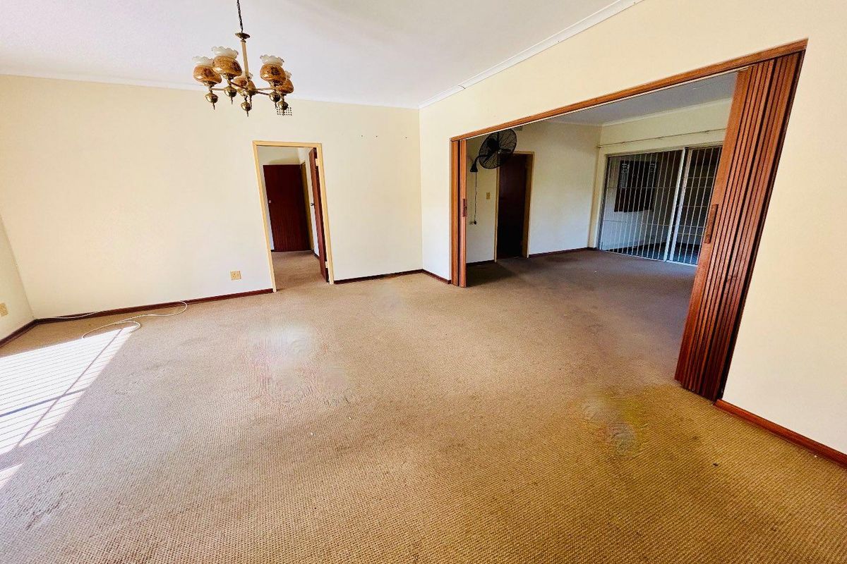 Spacious living area featuring neutral walls, carpeted flooring, and a folding room divider leading to an adjacent space with security gates.