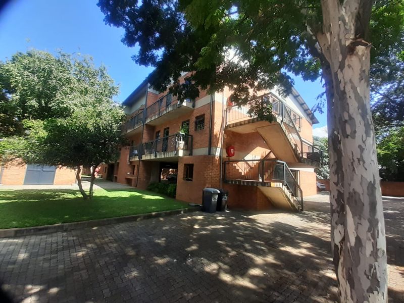 Exterior view of a multi-story brick apartment building featuring external staircases, private balconies, and a paved driveway area.