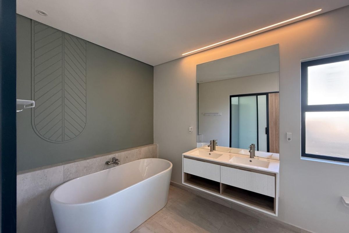 Modern bathroom featuring a sleek freestanding bathtub, double vanity with integrated storage, large mirror, and sophisticated decorative wall paneling with ambient lighting.