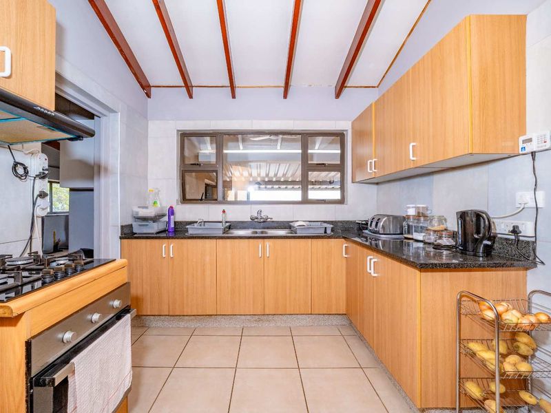 A functional kitchen featuring light wood cabinetry, granite countertops, a gas hob, and exposed ceiling beams, providing a practical workspace.