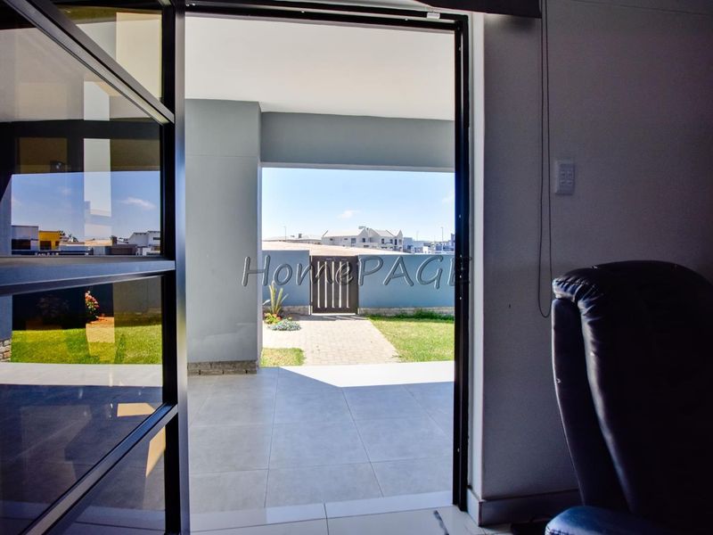 A view from an interior space looking out onto a covered patio area with tiled flooring, leading to a paved garden path.