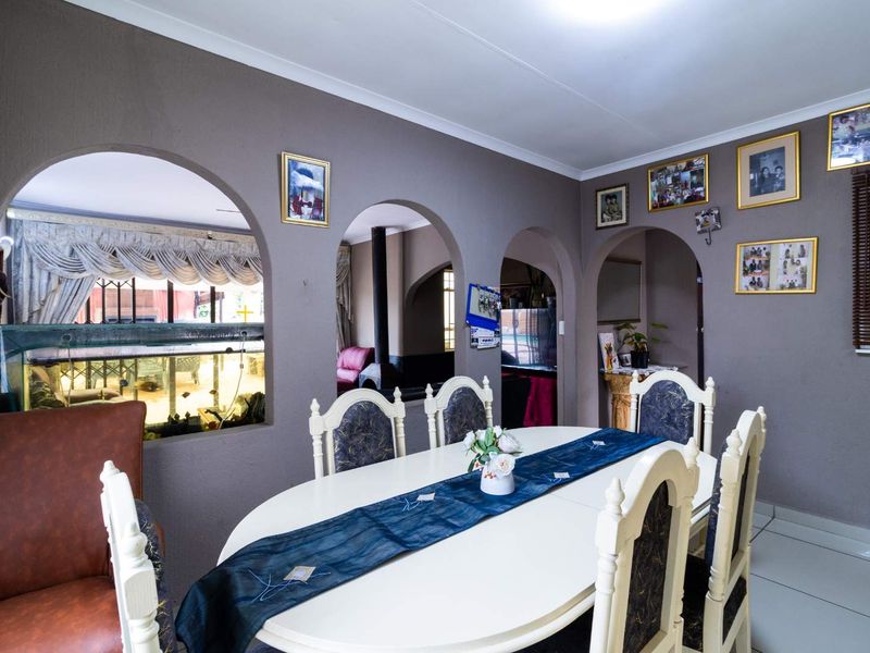A dining room featuring distinctive arched wall openings that provide views into adjacent living spaces, finished with tiled flooring and coved ceiling cornices.