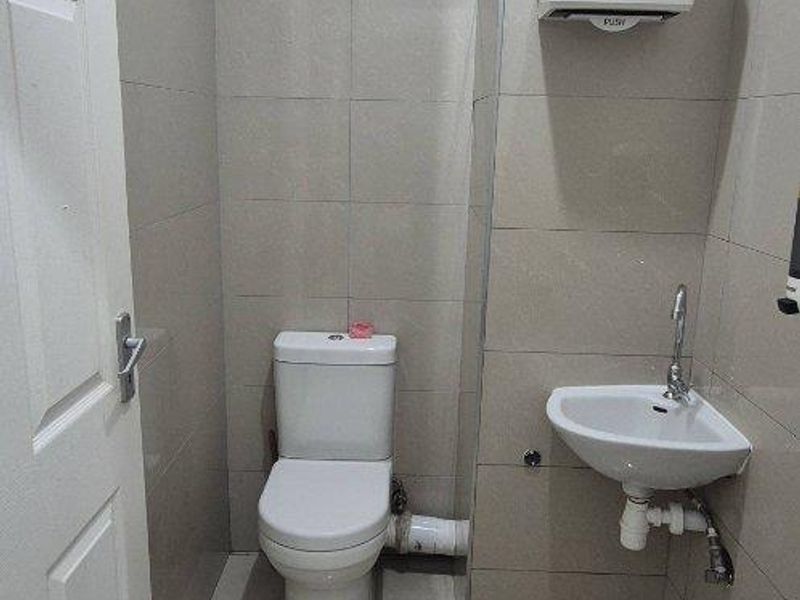 A compact office restroom featuring floor-to-ceiling tiling, a wall-mounted basin, and a standard toilet suite.
