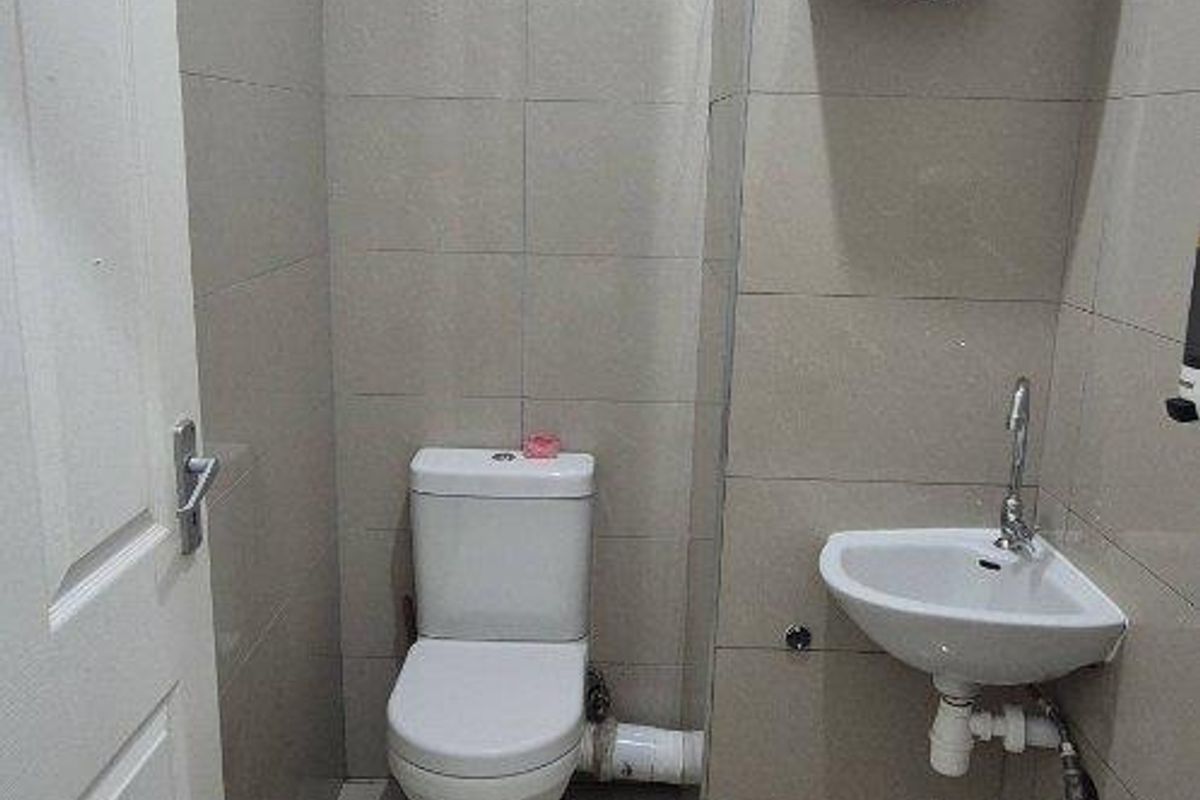A compact office restroom featuring floor-to-ceiling tiling, a wall-mounted basin, and a standard toilet suite.
