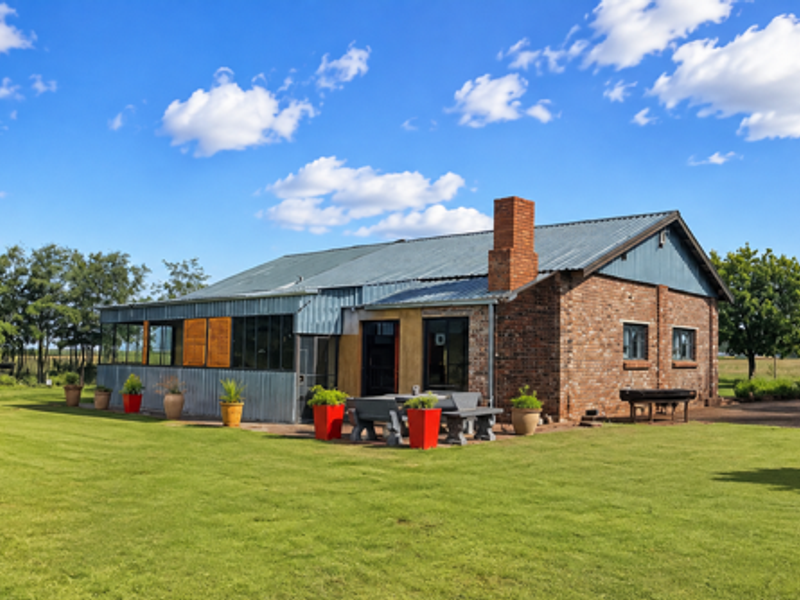 Rear view of a charming farm-style residence featuring a combination of exposed brick and corrugated metal cladding with an attached paved patio area.