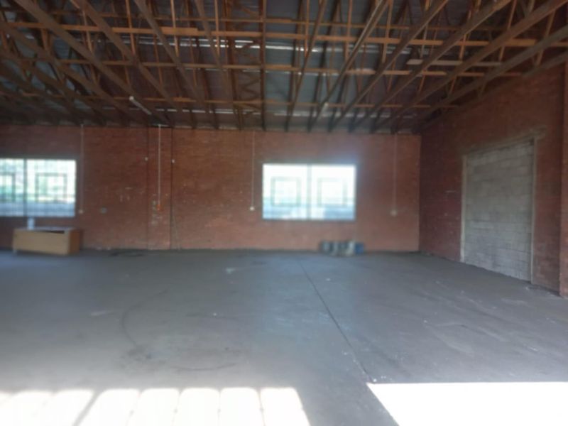 Spacious industrial utility area featuring exposed timber roof trusses, brick walls, and concrete flooring, suitable for workshop or storage use.