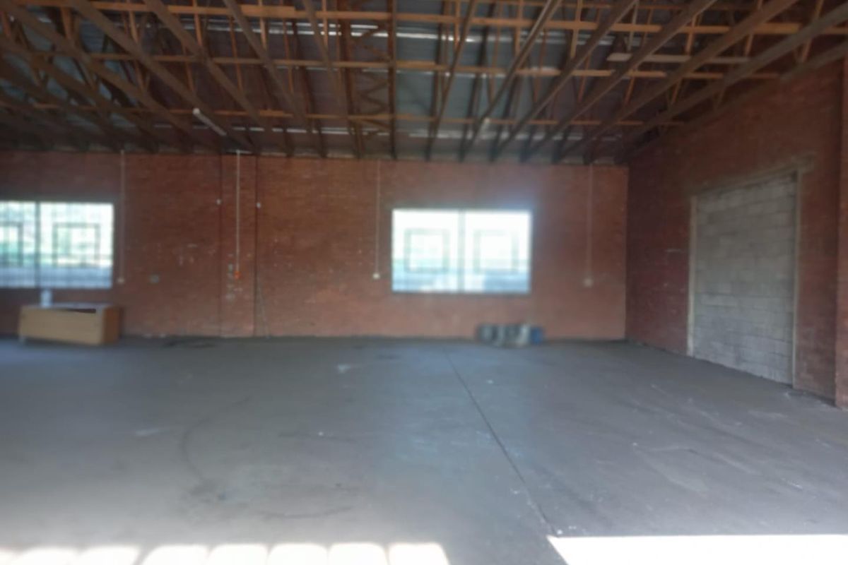 Spacious industrial utility area featuring exposed timber roof trusses, brick walls, and concrete flooring, suitable for workshop or storage use.