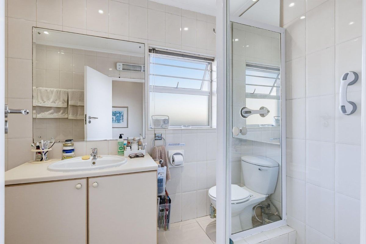 A functional bathroom featuring a vanity with basin, wall-mounted mirror, toilet, and a separate shower enclosure with tiled walls.