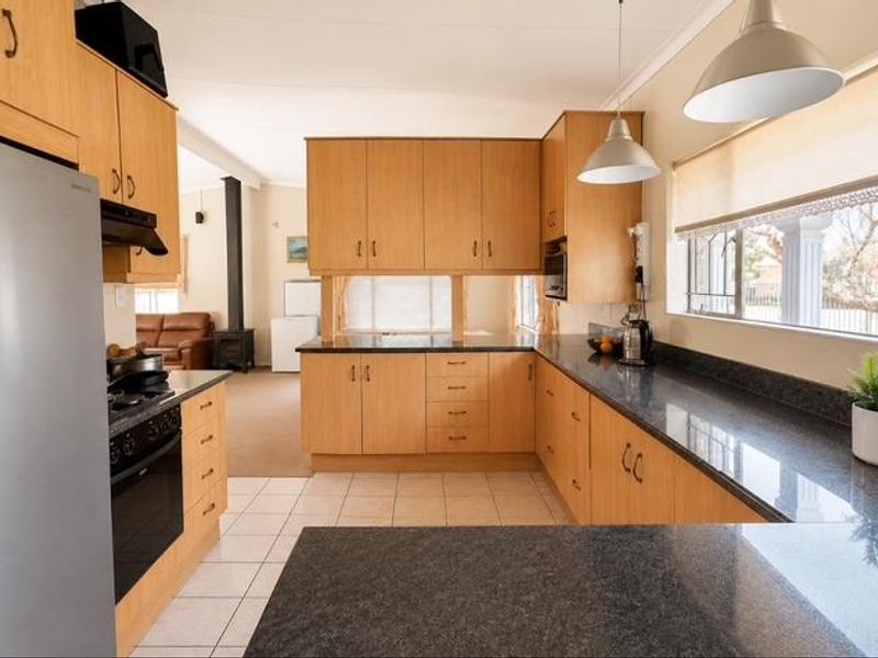 Functional kitchen featuring light wood cabinetry, dark granite countertops, built-in oven and hob, and tiled flooring, with an open-plan layout leading to the living area.