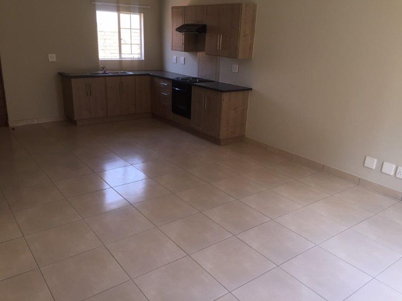 An open-plan kitchen area featuring light wood-finish cabinetry, dark countertops, and neutral ceramic floor tiles in a clean, vacant space.