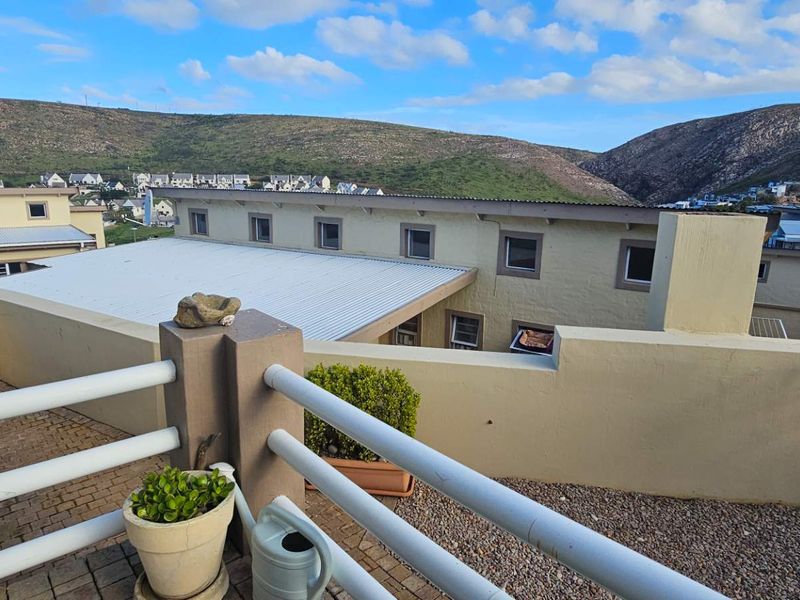 An elevated balcony with metal railings and paved flooring, offering expansive views of the surrounding estate and hillside landscape.
