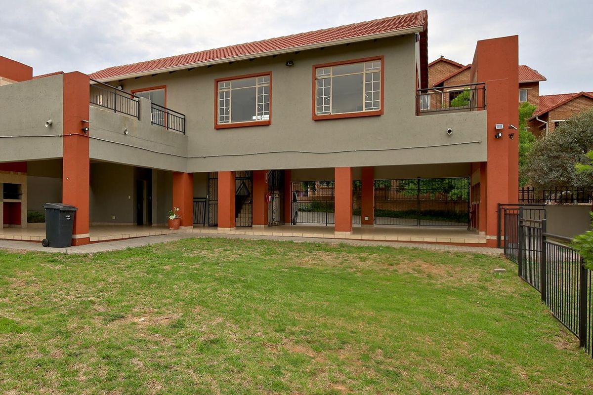 Rear view of the apartment building featuring a covered patio with a built-in braai, tiled flooring, and access to a private garden area.
