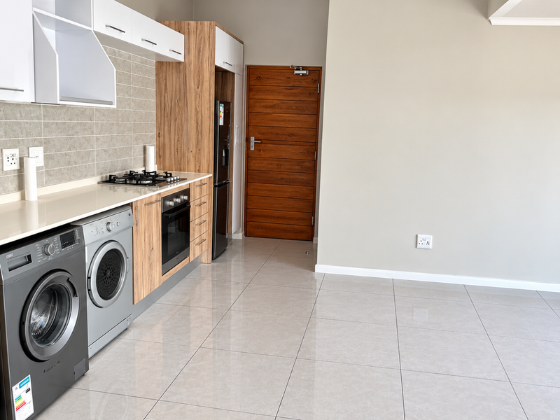 Modern kitchen featuring sleek wood-grain cabinetry, stone countertops, gas hob, built-in oven, and polished porcelain floor tiles in an open-plan layout.