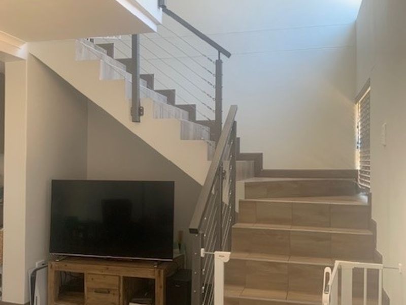 A living area featuring a modern staircase with tiled treads and a metal balustrade, complemented by matching tiled flooring throughout the space.