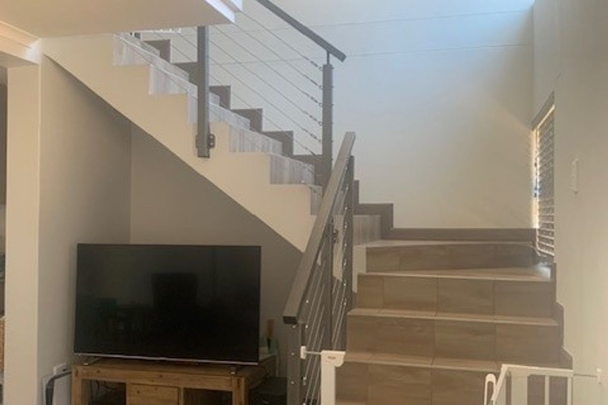 A living area featuring a modern staircase with tiled treads and a metal balustrade, complemented by matching tiled flooring throughout the space.