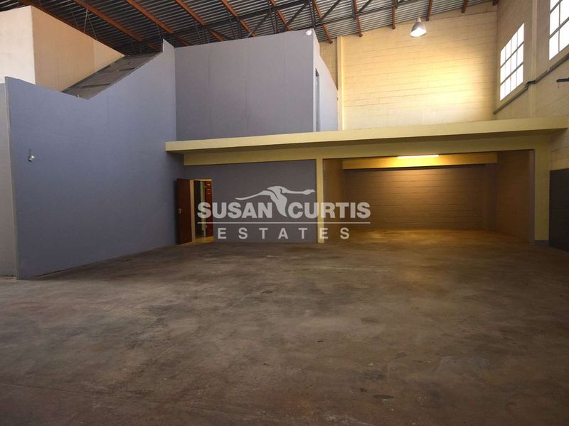 Spacious industrial warehouse unit featuring high ceilings with exposed steel trusses, a mezzanine level, and durable concrete flooring.
