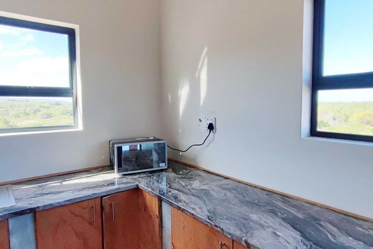 A functional kitchen area featuring modern laminate countertops, wooden cabinetry, and large windows offering scenic landscape views.