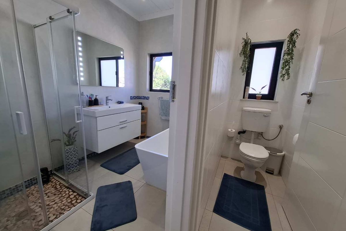 Modern bathroom featuring a glass-enclosed shower with pebble flooring, a sleek wall-mounted vanity, a freestanding bathtub, and a separate toilet area.