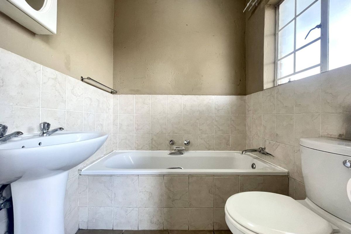 A dated bathroom featuring a pedestal basin, a built-in bathtub with tiled surround, and a standard toilet.