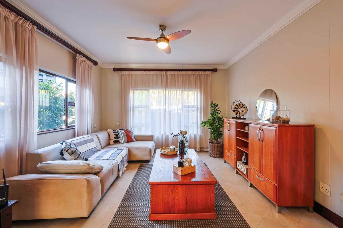 A comfortable living room featuring tiled flooring, crown molding, and a ceiling fan, providing a bright and inviting space for relaxation.