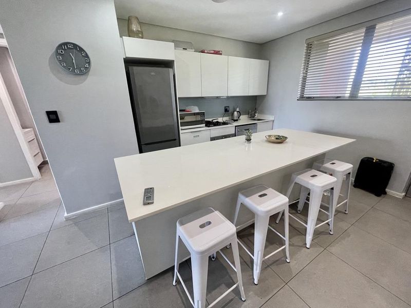 Modern kitchen featuring a large central island with quartz countertops, sleek white cabinetry, tiled flooring, and integrated cooking appliances.
