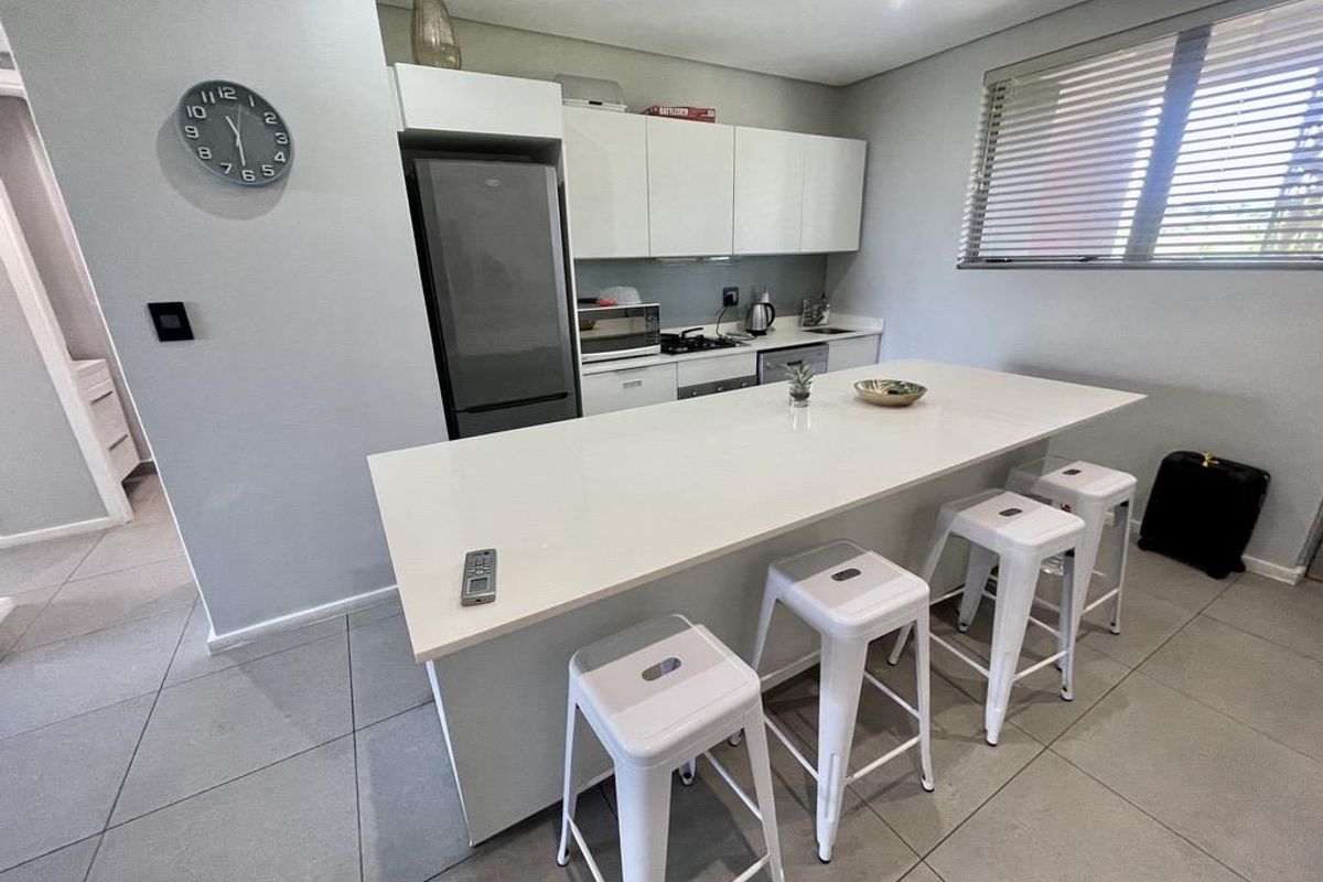 Modern kitchen featuring a large central island with quartz countertops, sleek white cabinetry, tiled flooring, and integrated cooking appliances.