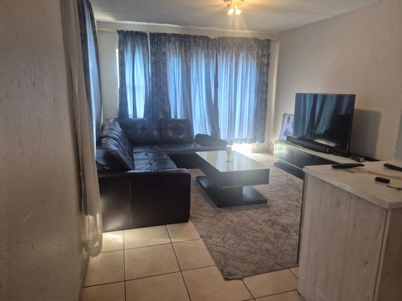 A living room area featuring tiled flooring and natural light access through large window curtains.