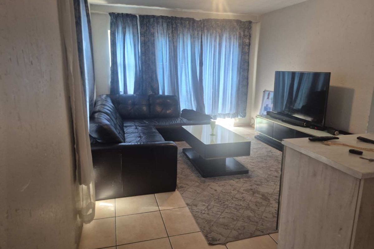 A living room area featuring tiled flooring and natural light access through large window curtains.