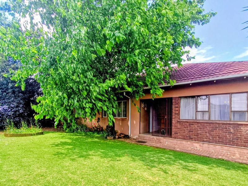 Rear view of the house featuring a brick facade, tiled roof, and large garden with mature trees.