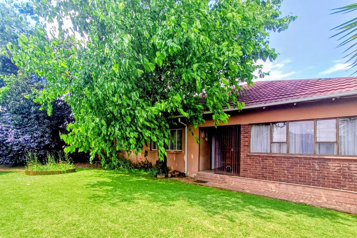 Rear view of the house featuring a brick facade, tiled roof, and large garden with mature trees.