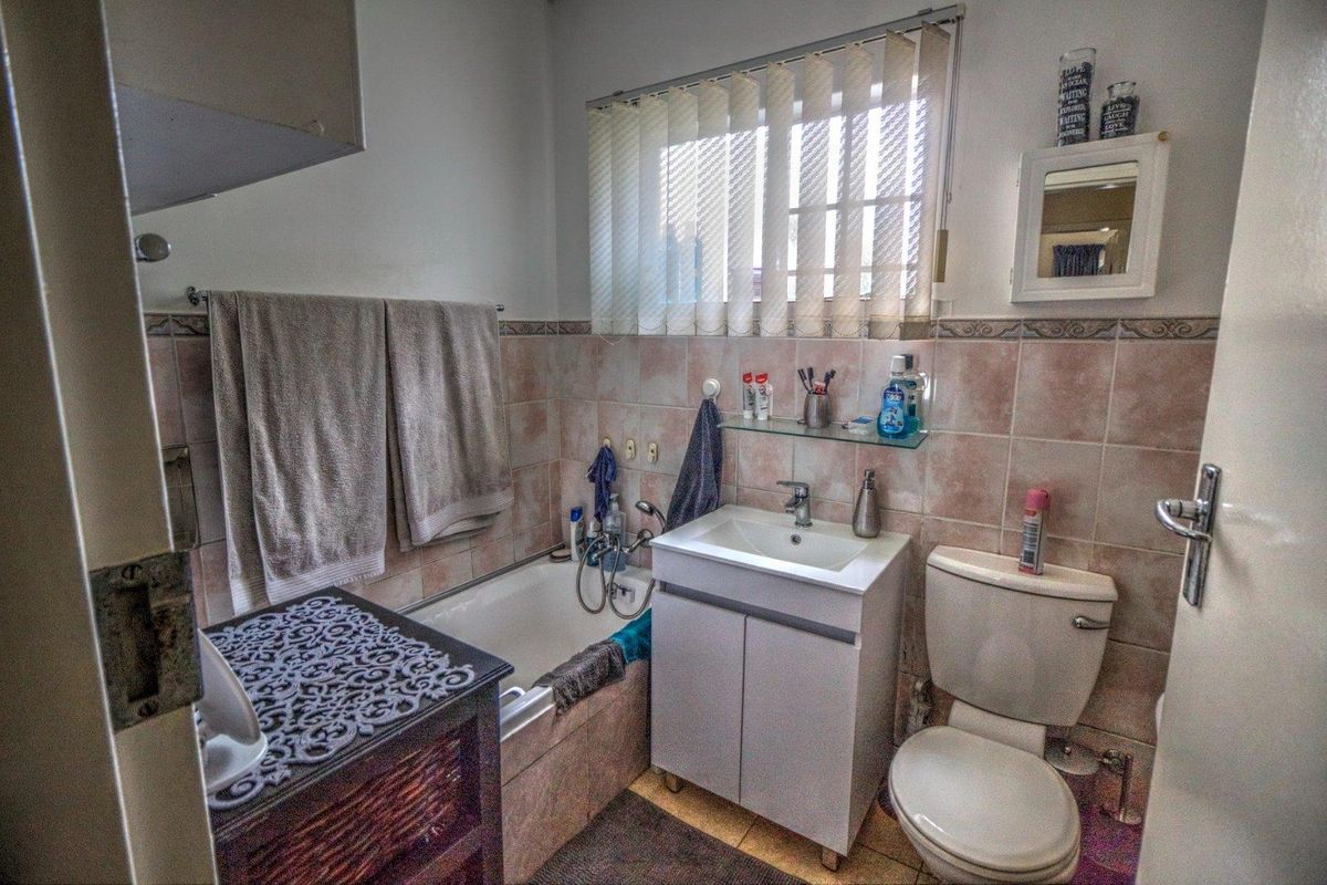 A functional bathroom featuring a built-in bathtub, vanity basin, and toilet with tiled walls and a window for natural light.