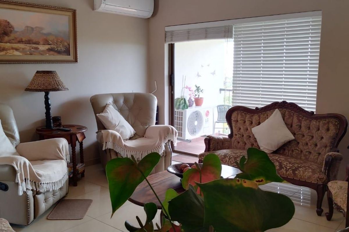 A comfortable living room featuring tiled flooring, a wall-mounted air conditioning unit, and large sliding glass doors leading to an outdoor balcony.