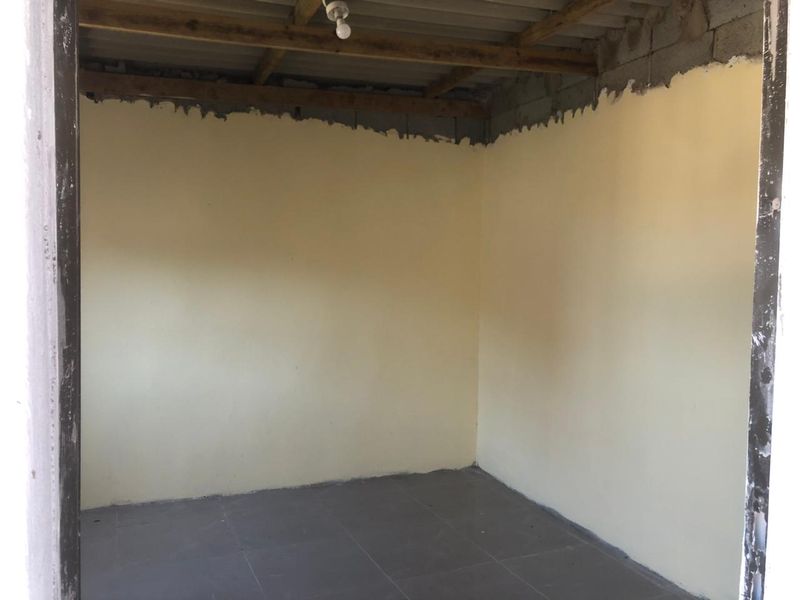 An unfinished interior room featuring tiled flooring, exposed timber roof beams, and partially plastered walls, offering a blank canvas for renovation.