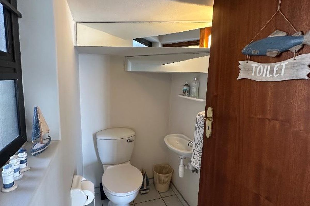 A compact guest bathroom featuring a toilet, wall-mounted basin, tiled flooring, and a built-in mirror shelf.