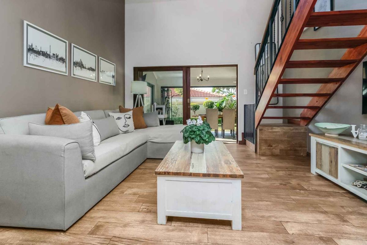 A bright living room featuring wood-look tile flooring, a feature staircase with wrought iron railings, and sliding glass doors leading to an outdoor patio area.