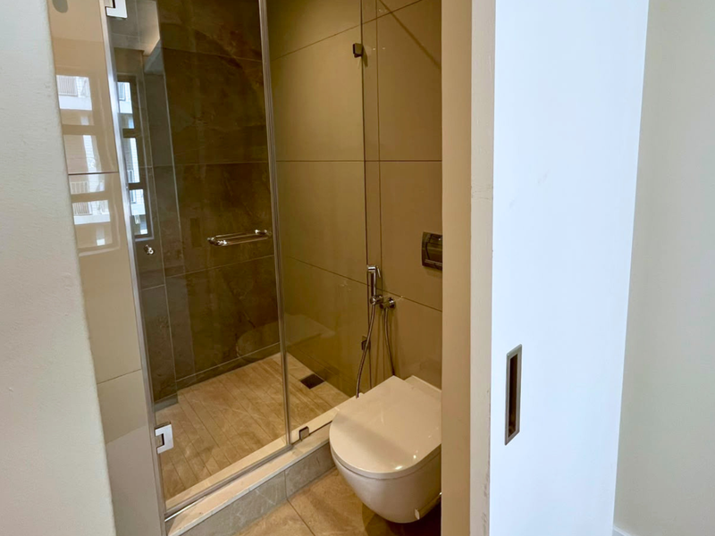 Modern bathroom featuring a glass-enclosed shower, wall-mounted toilet with bidet spray, and neutral-toned wall tiles.