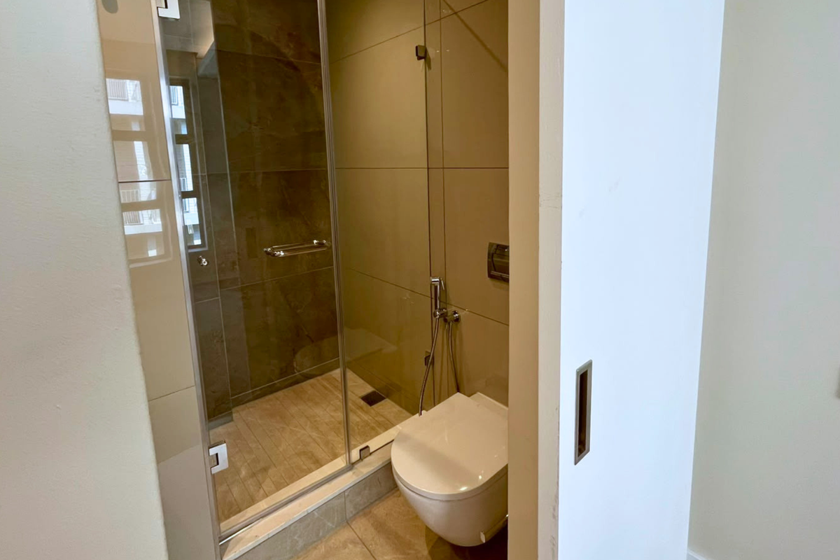 Modern bathroom featuring a glass-enclosed shower, wall-mounted toilet with bidet spray, and neutral-toned wall tiles.