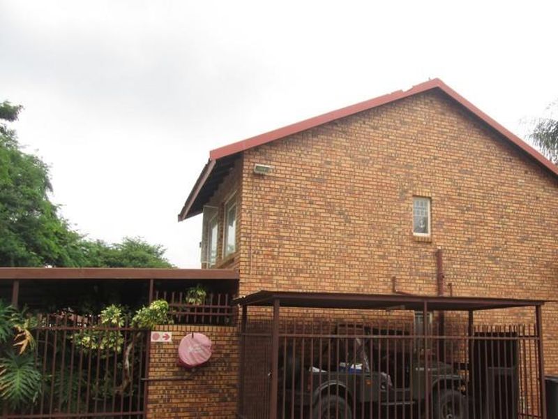 Exterior view of a face brick apartment building featuring a metal carport and secure perimeter fencing.