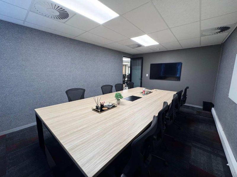 A professional office boardroom featuring a large meeting table, suspended ceiling with recessed lighting, and dark carpeted flooring.