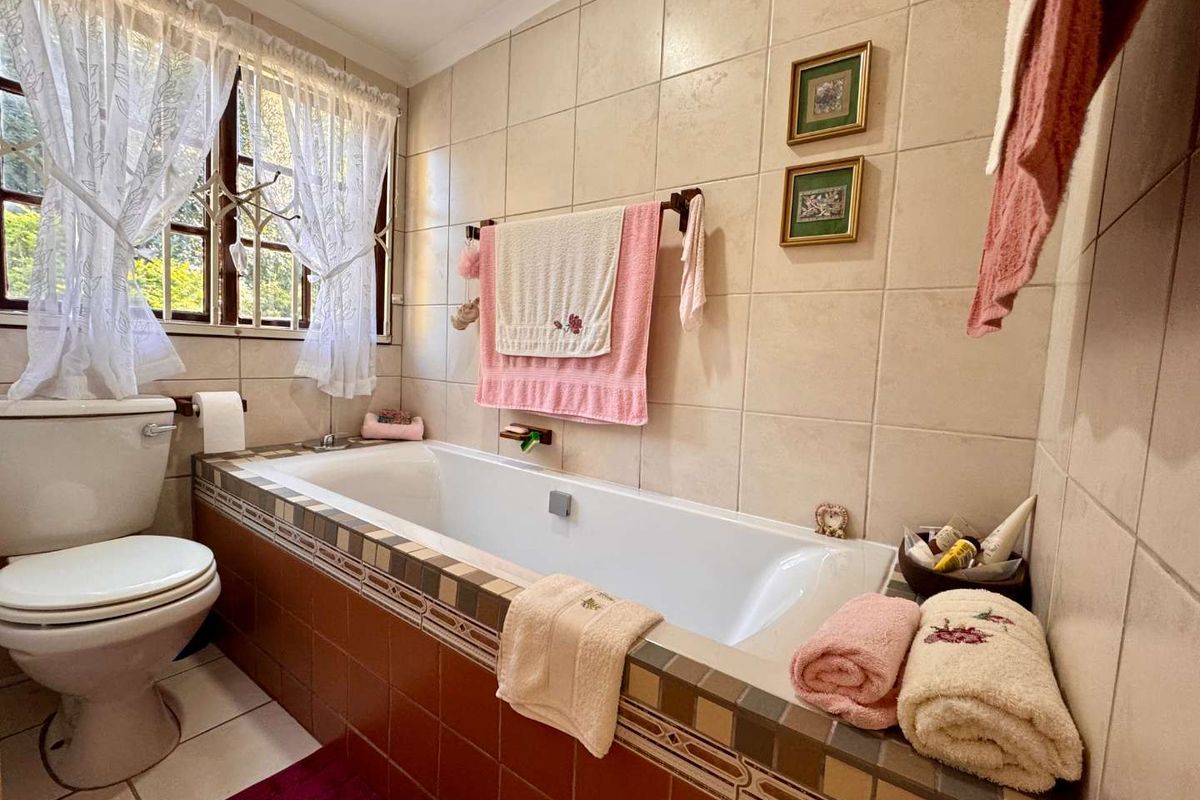 A functional bathroom featuring a built-in bathtub with decorative tile surround, a standard toilet, and tiled walls.