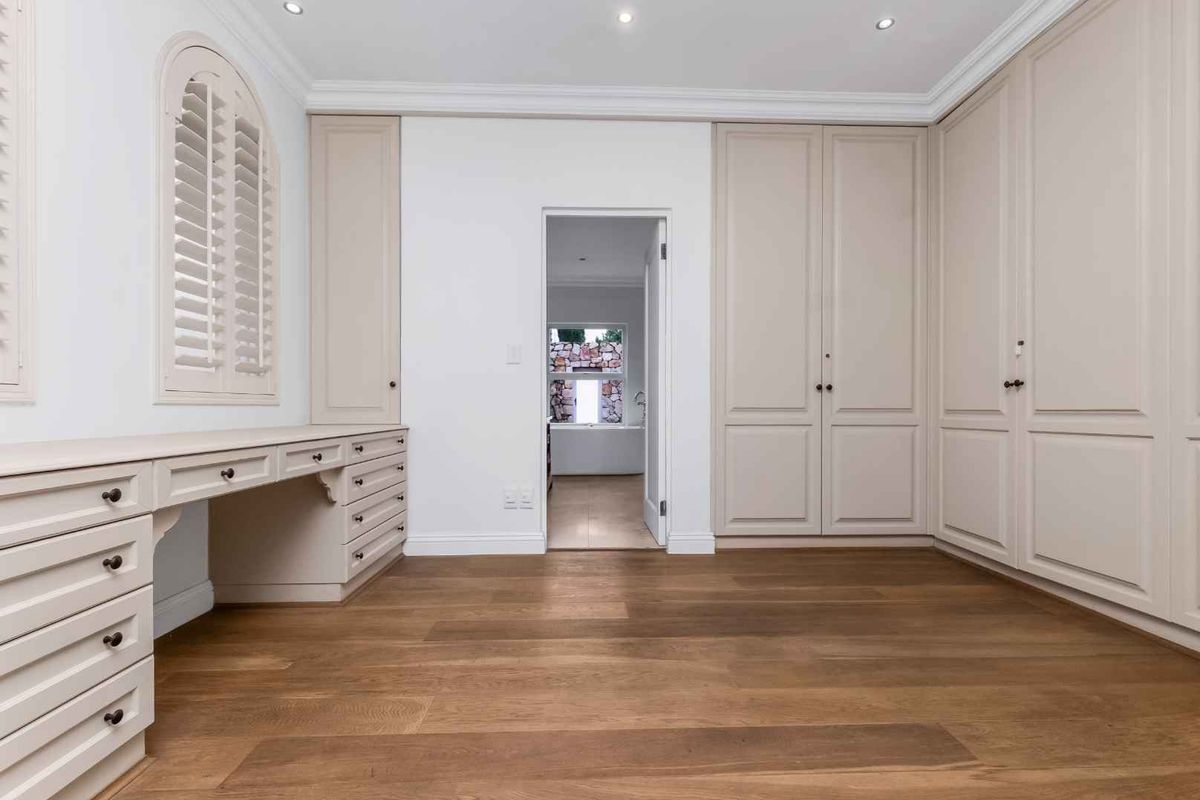 A bright, well-maintained bedroom featuring extensive built-in cabinetry, a custom desk area, hardwood flooring, and elegant crown molding.