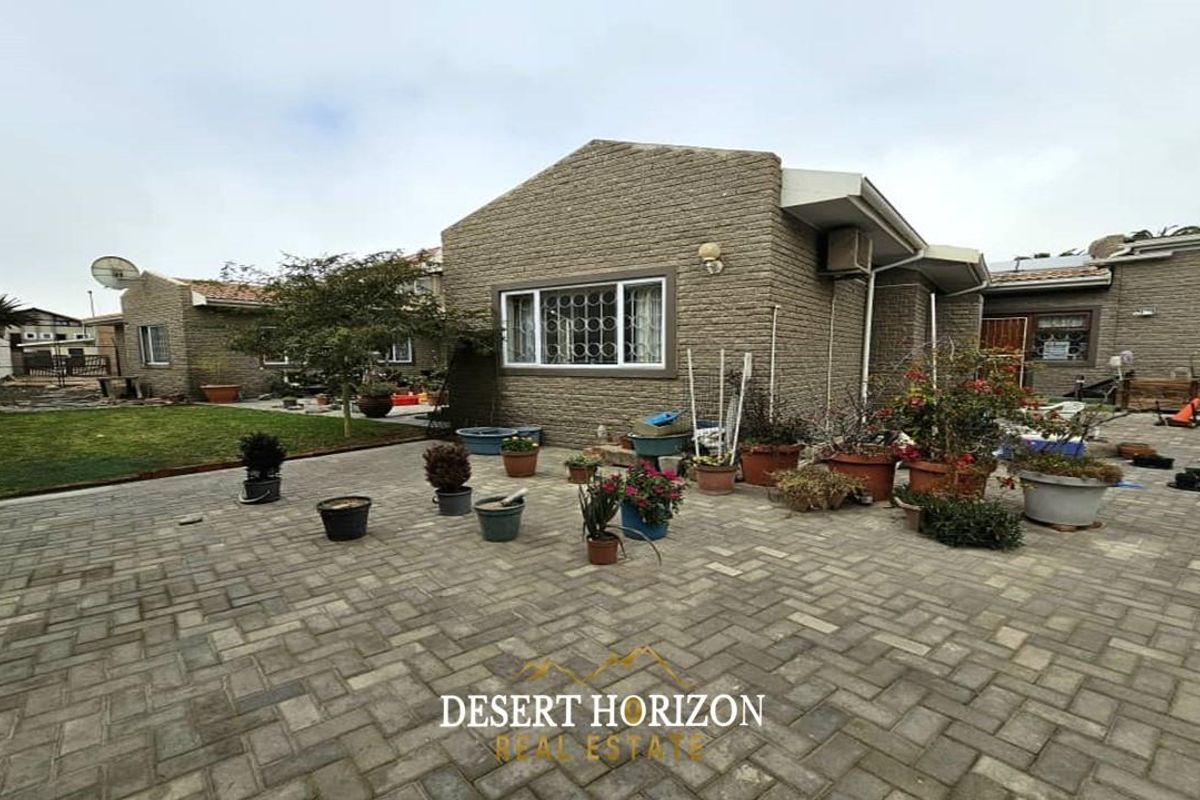 A spacious rear exterior area featuring paved courtyard space, a small lawn, and brick-clad building facades.