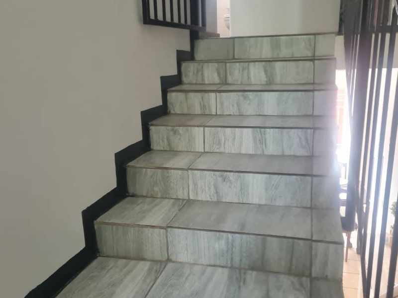A staircase featuring light-toned tiled steps and a black metal balustrade, providing access between levels within the apartment.
