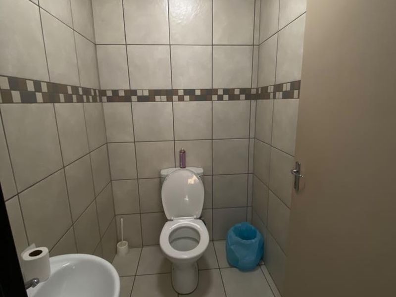 A compact functional bathroom featuring full-height ceramic wall tiling, a standard toilet, a small washbasin, and an integrated extractor fan.
