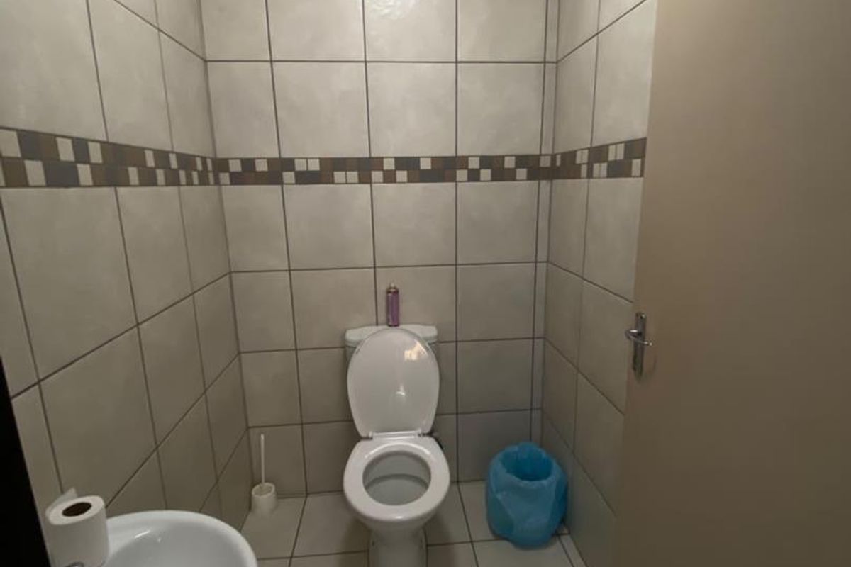 A compact functional bathroom featuring full-height ceramic wall tiling, a standard toilet, a small washbasin, and an integrated extractor fan.