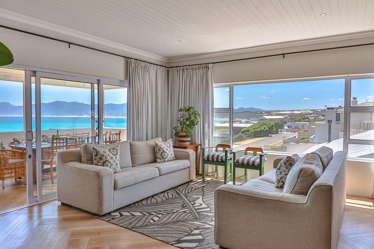 Bright living room featuring herringbone timber flooring, tongue-and-groove ceiling, and expansive sliding glass doors opening to a scenic balcony with coastal views.