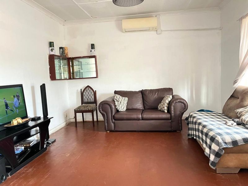 A living room featuring a wall-mounted air conditioning unit, built-in wall cabinetry, and coved ceilings, with worn flooring throughout.