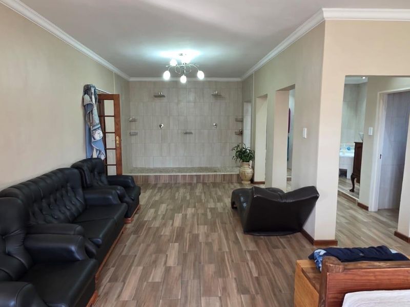 Spacious living area featuring wood-look tiled flooring, cove ceiling, and an unusual integrated dual shower installation against the rear wall.