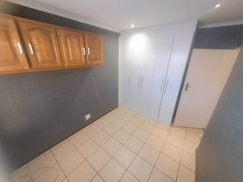An empty bedroom featuring tiled flooring, built-in white wardrobes, and additional wall-mounted wooden storage cabinets.