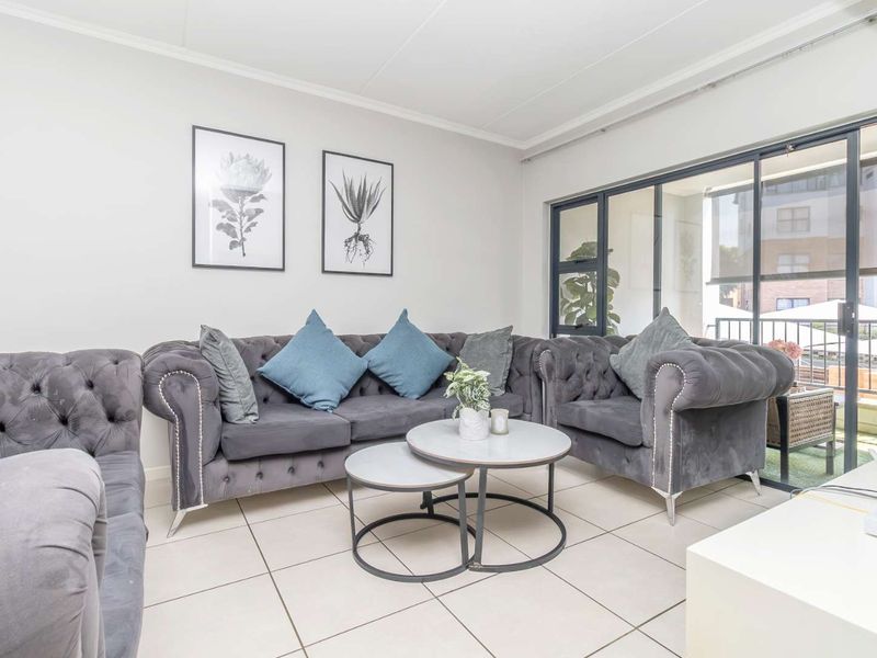 A bright living room featuring neutral tiled flooring and large sliding glass doors that provide access to an outdoor balcony area.